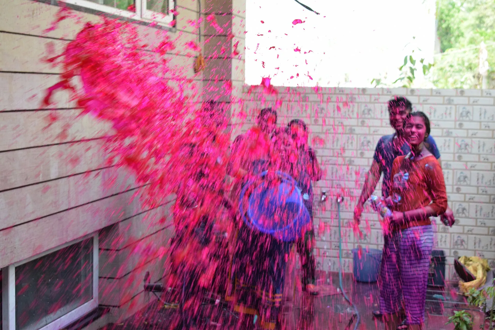People throwing bright pink coloured water over each other during Holi