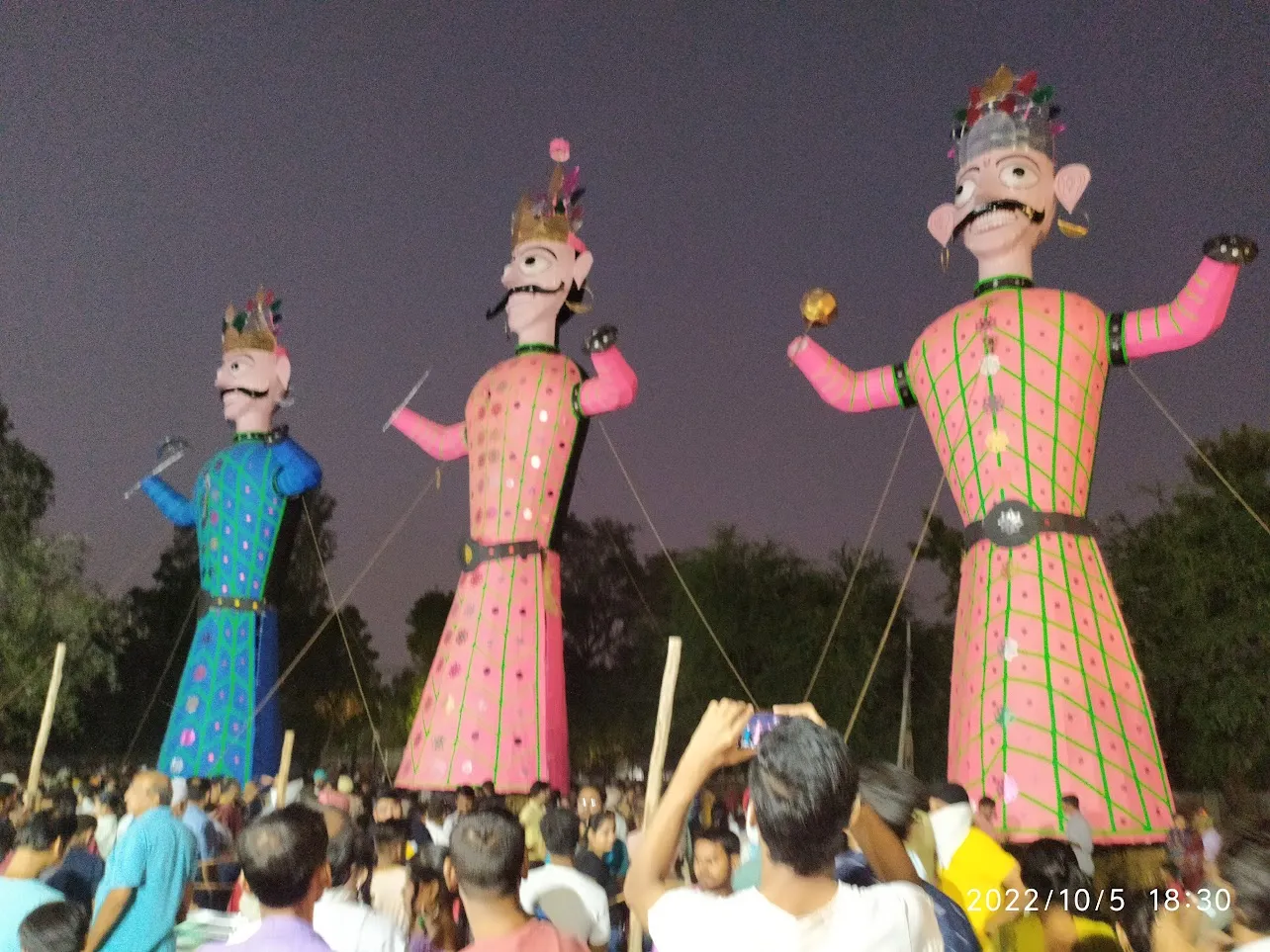 Three towering colourful effigies of Ravana and his kin before a Dussehra crowd at dusk