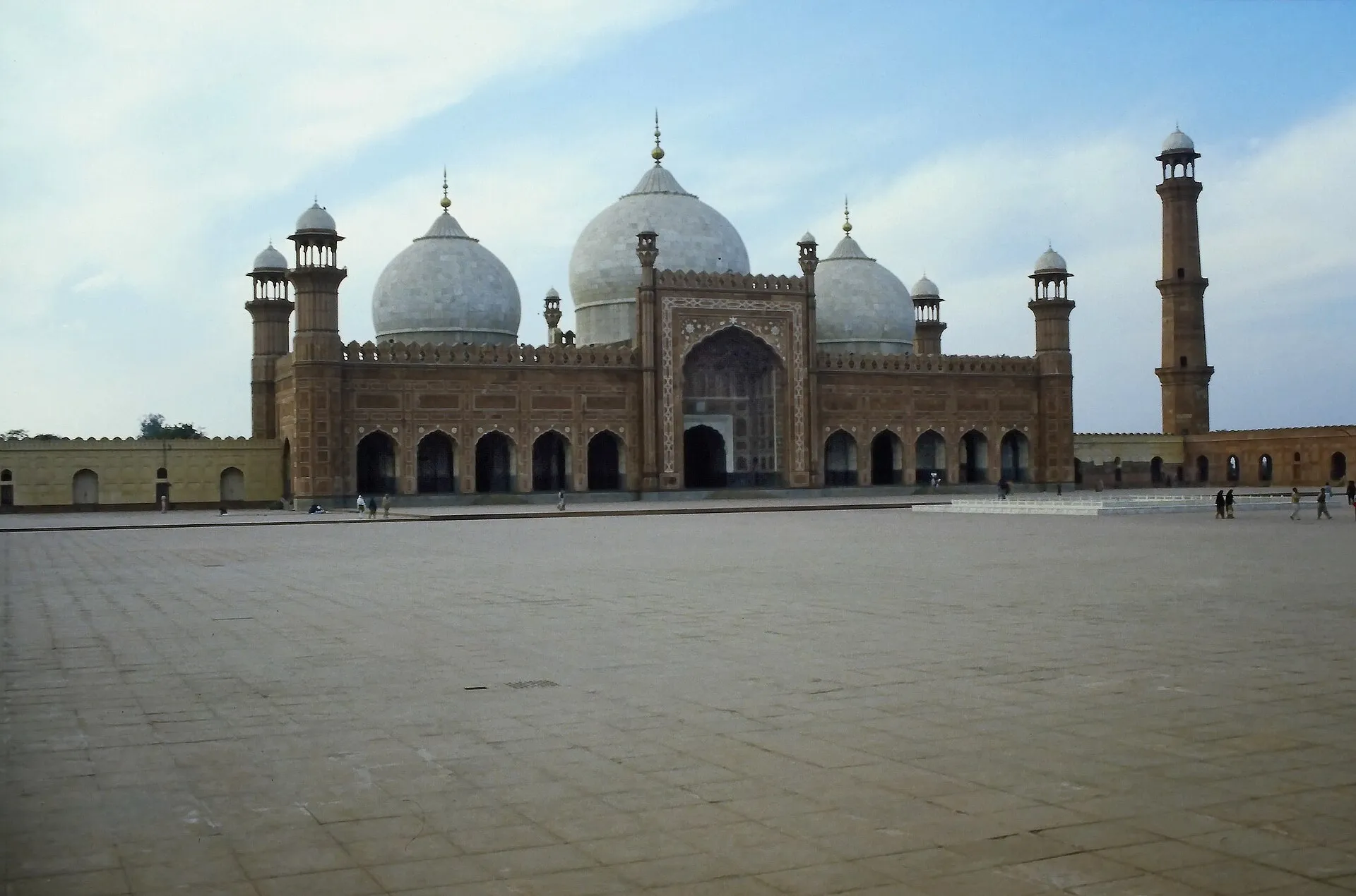 The Badshahi Mosque in Lahore seen across its vast courtyard, three white marble domes above red sandstone