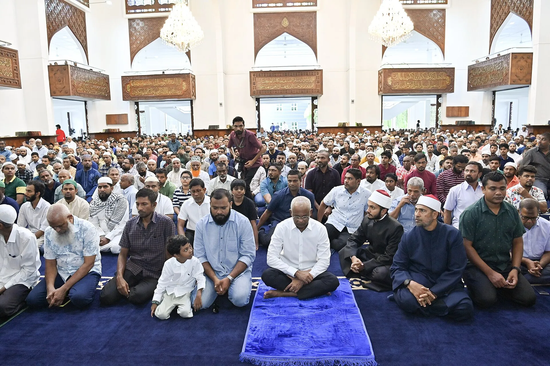 Rows of worshippers seated inside a bright mosque hall during Eid al-Adha prayers