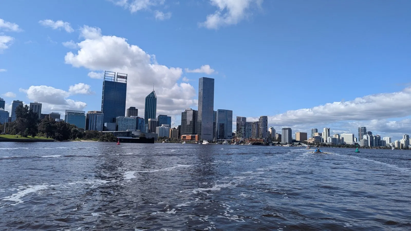 Perth city skyline seen across the Swan River under a blue sky with white clouds