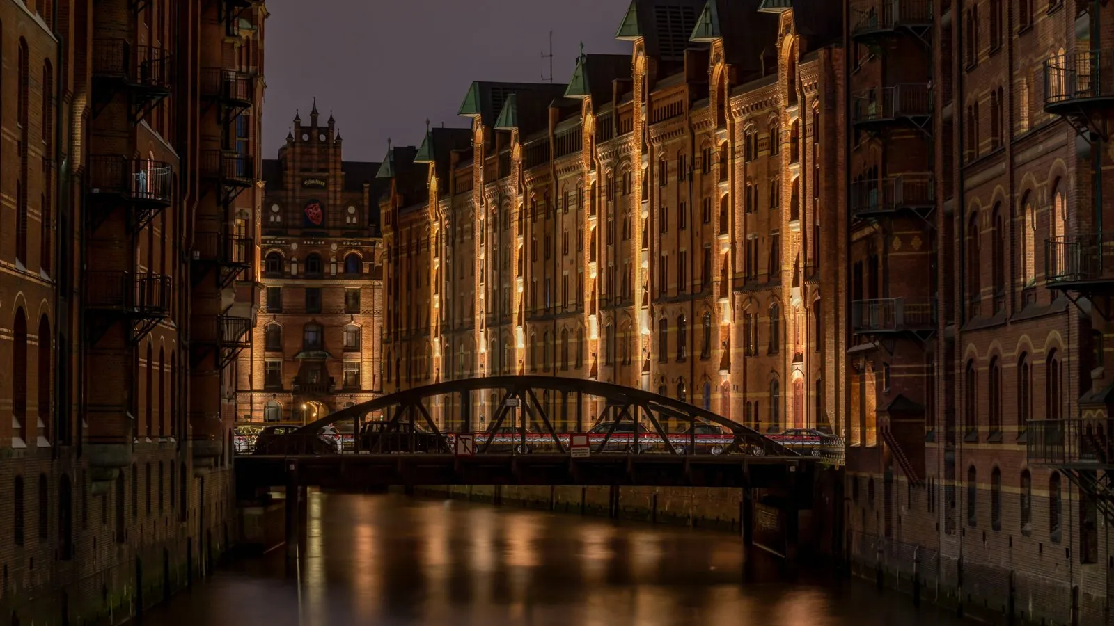 The Speicherstadt warehouse district in Hamburg at night, red brick warehouses lit along a canal with a bridge in the foreground