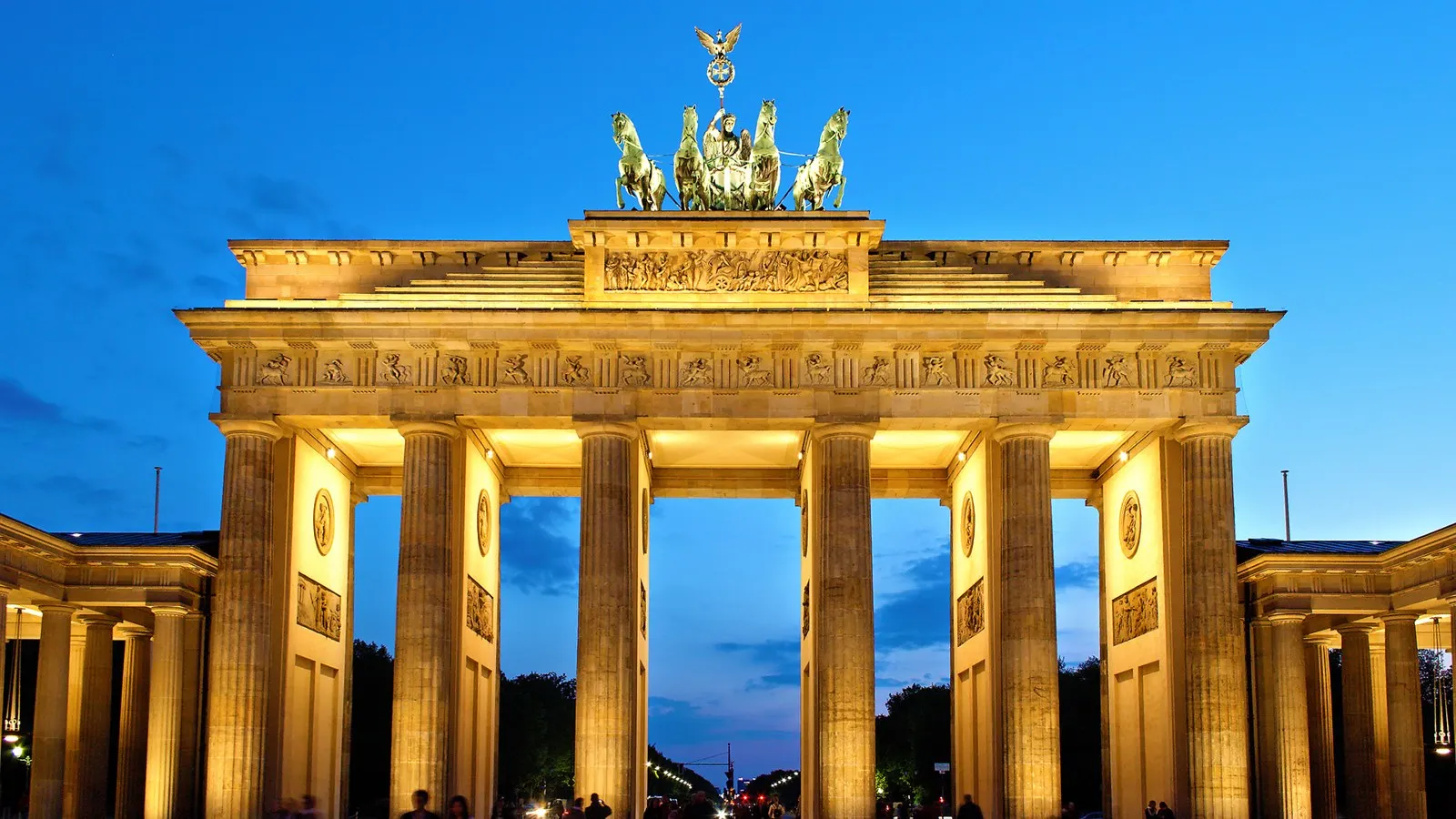 The Brandenburg Gate in Berlin at dusk, its columns and Quadriga lit gold against a deep blue sky